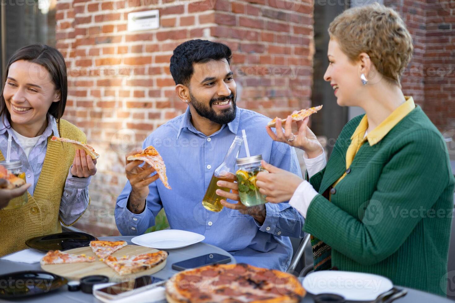 Friends enjoy pizza and drinks outdoors at a restaurant, creating a scene of social gathering and leisure. photo