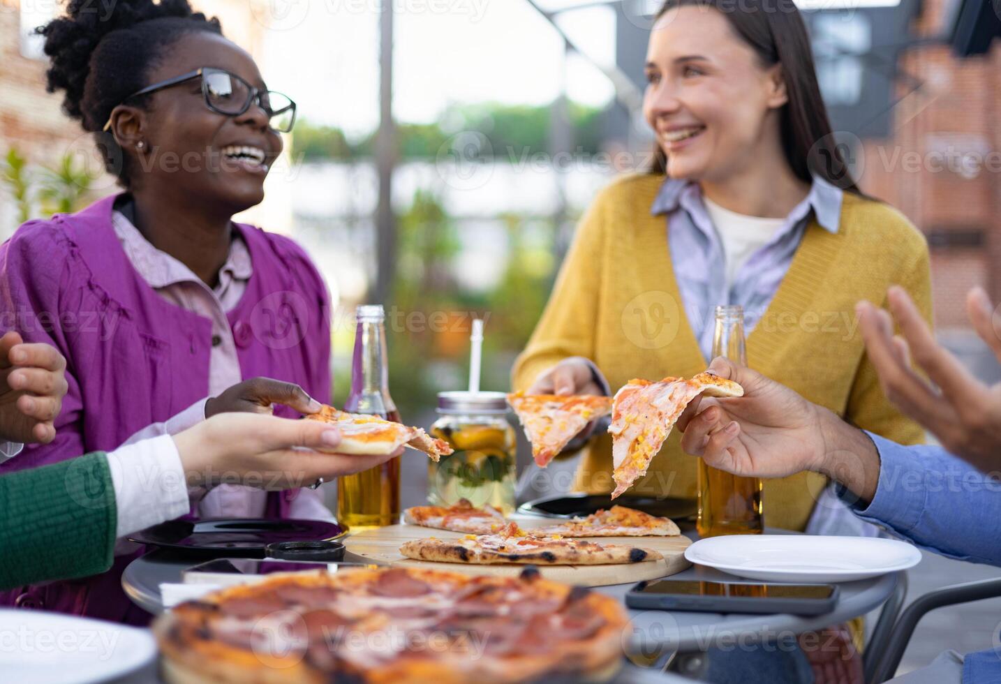 Friends sharing pizza outdoors, laughing and enjoying each other's company at a table. photo