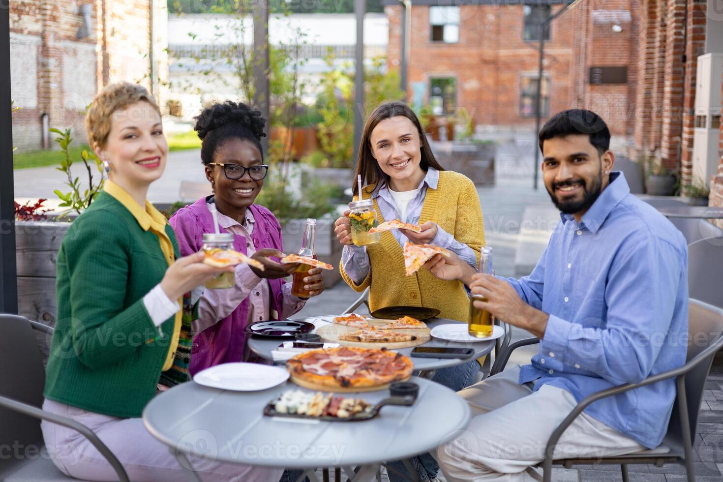 Diverse group of friends enjoying pizza and drinks together outdoors at a restaurant. photo
