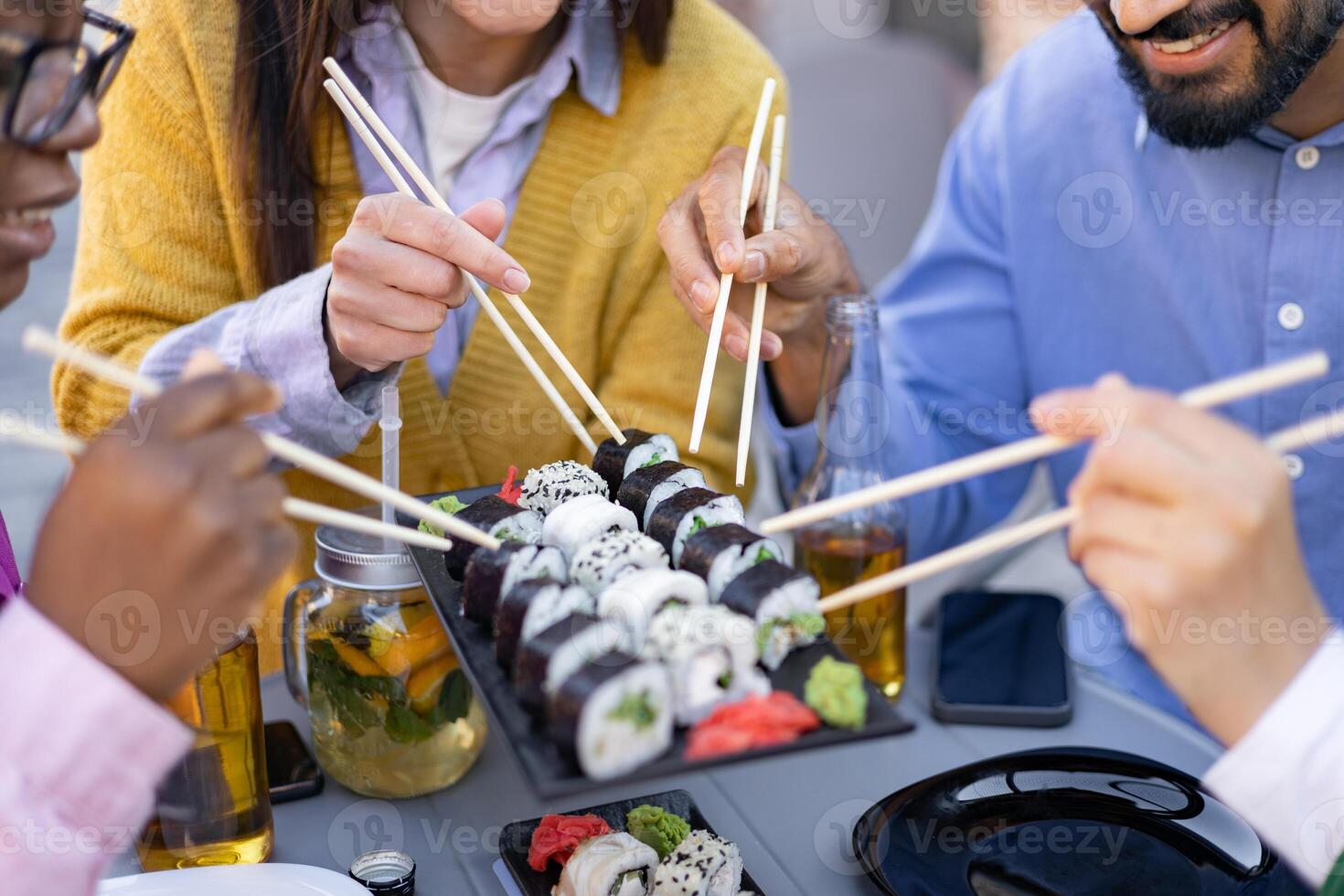 A group of friends enjoys a delicious sushi meal outdoors, using chopsticks to savor various sushi rolls. photo
