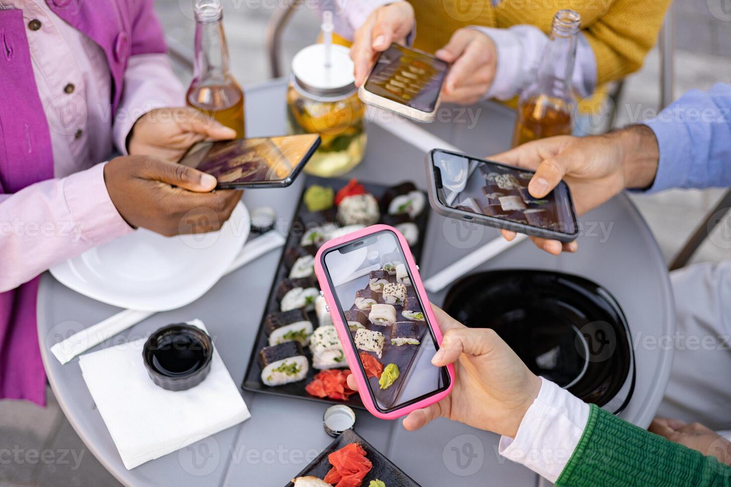 Friends gather at a table to take photos of sushi with their smartphones, capturing the moment of their meal together.