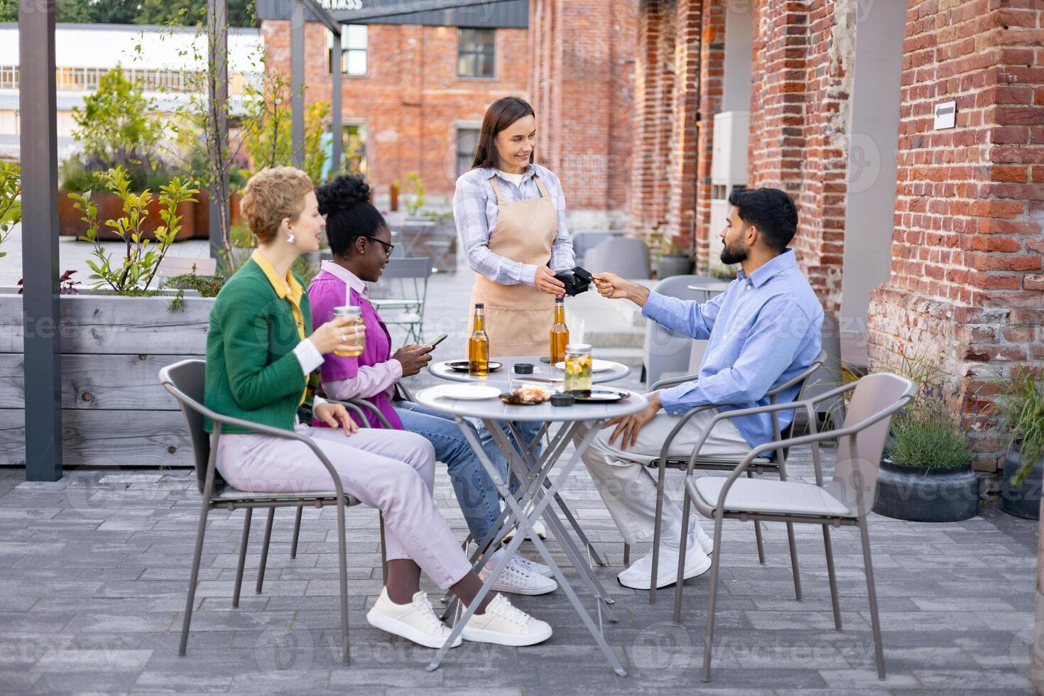 A female waiter at an outdoor cafe uses a portable terminal to process a customer's payment. photo