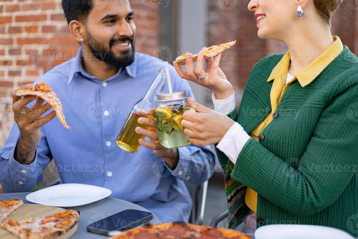 A couple shares pizza and drinks on an outdoor table, enjoying a meal together. photo