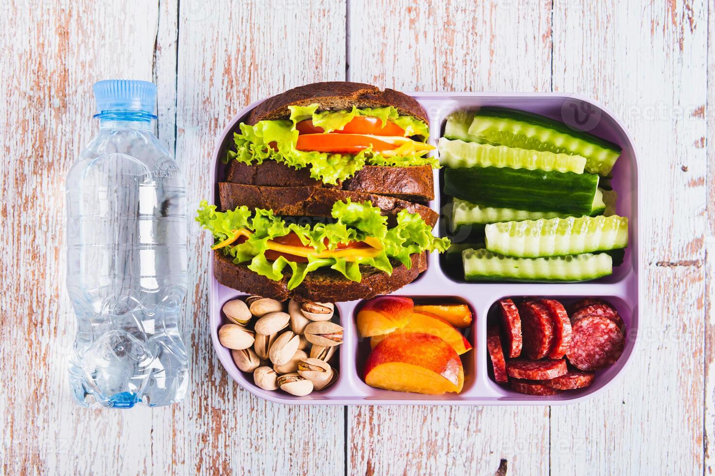Close up lunch box with food, bottle of water on the table top view photo