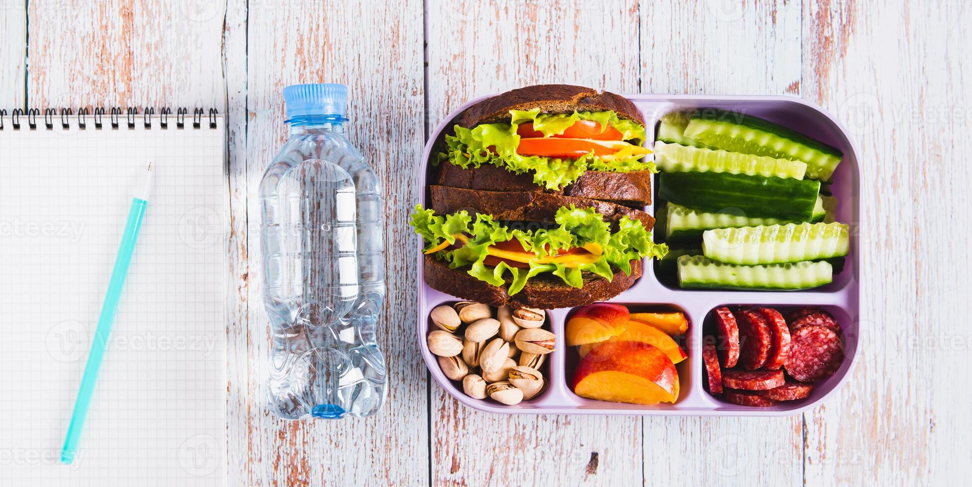 Lunchbox with sandwich, chorizo, cucumber and peach, bottle of water top view web banner photo