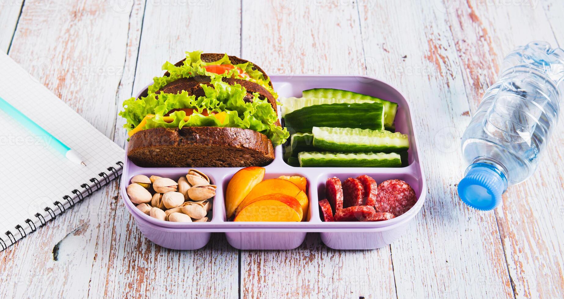 Lunch box with food, bottle of water, notebook and pen on the table web banner photo