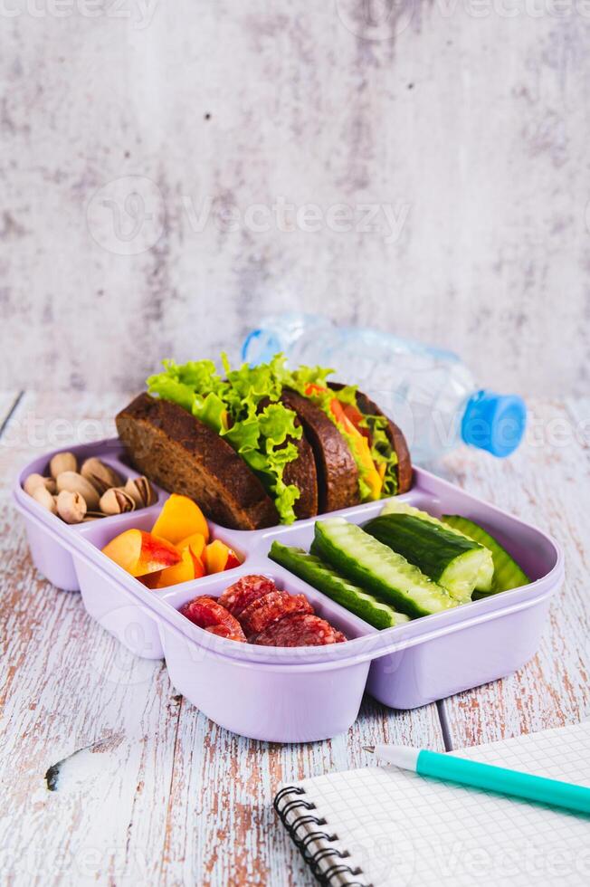 Lunch box with food, bottle of water, notebook and pen on the table vertical view photo