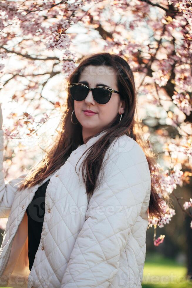 Young woman enjoying springtime under cherry blossom trees during a sunny afternoon in a park setting photo