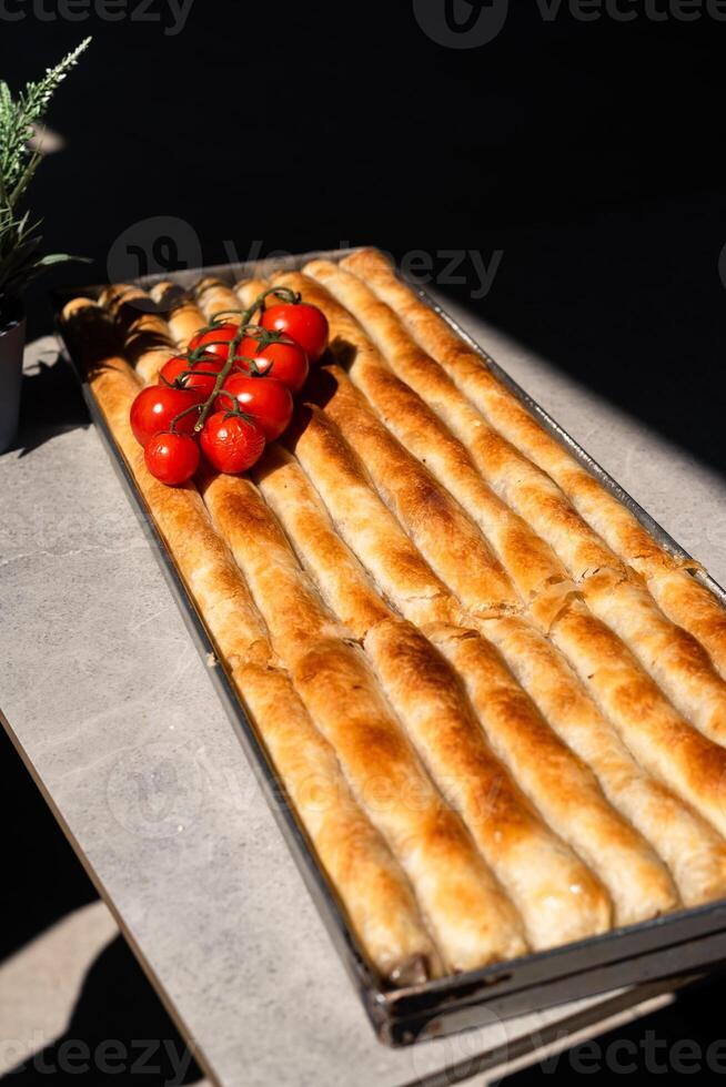 Traditional pastry - pie with cheese - pita served in a baking tray, topped with fresh cherry tomatoes with natural daylight. photo