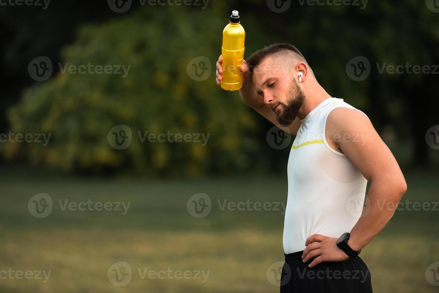 Tired male athlete or fit man cooling down with a water bottle after outdoor workout or run in the park. Active lifestyle. photo