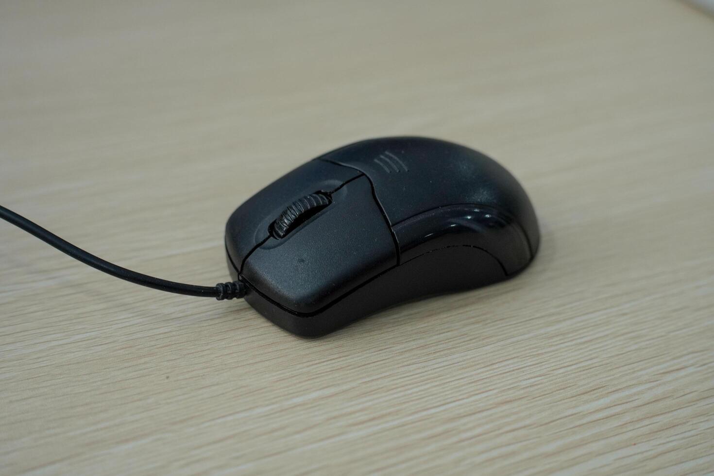 A close-up photo of a wired black computer mouse placed on desk. The image suitable for illustrating technology, computer equipment, or workplace themes