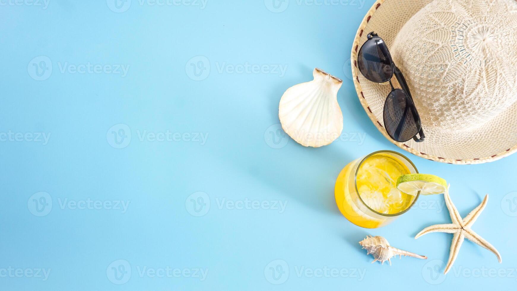 Cold refreshing summer beverage lemon or orange drink with ice cubes and a summer hat and sunglasses isolated on blue background for summer concept photo