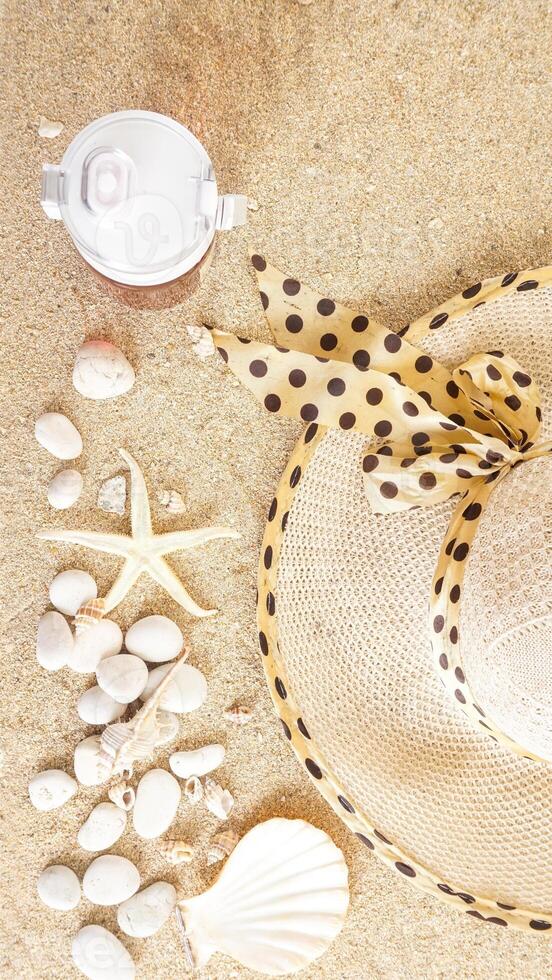 Top view flat lay of summer holiday concept with summer hat, a drink tumbler, and sea creatures isolated on beach sand background photo