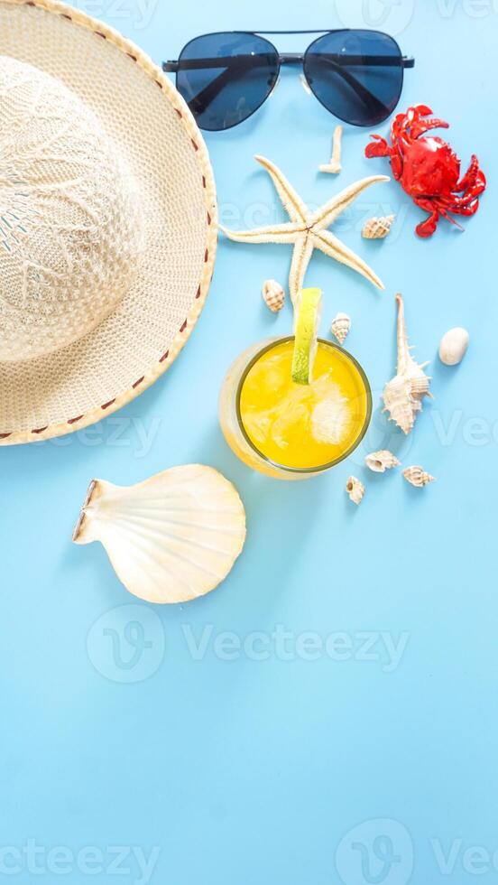 Flat lay arranged of summer concept with a glass of cold refreshing summer drink, sunglasses, summer hat, sea shells, starfish, and crab miniature isolated on blue background photo