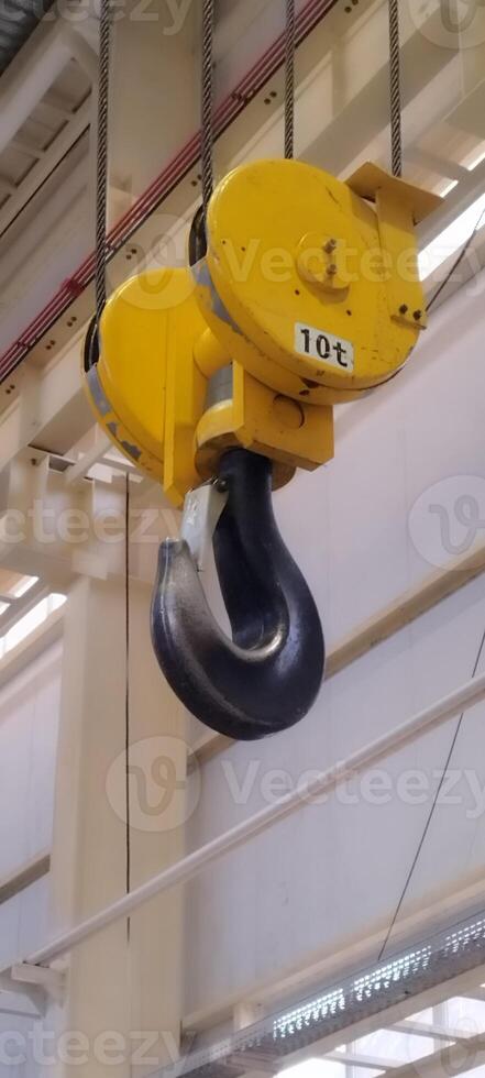 Heavy-duty crane hook with a 10-ton capacity. Yellow hoist and black steel hook. Industrial equipment for lifting heavy loads. Large industrial crane hook with safety catch, suspended in the workshop. photo