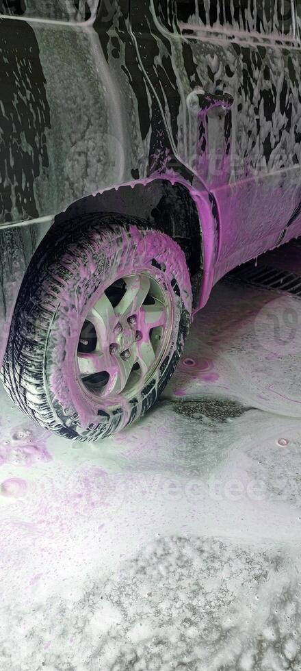 Car wash close-up with white and vibrant pink foam covering the vehicle. Cleaning process. Self-service station, no people. Perfect for auto care, maintenance, and service concepts. Advertising. photo