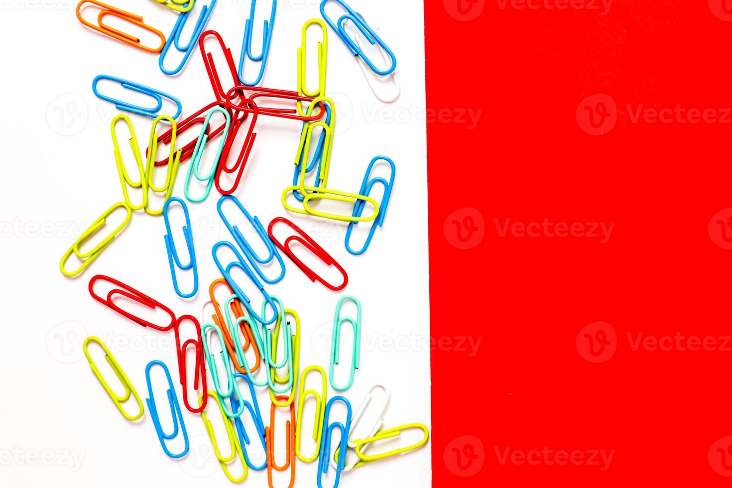Colorful paper clips on white and red background, office or school concept photo