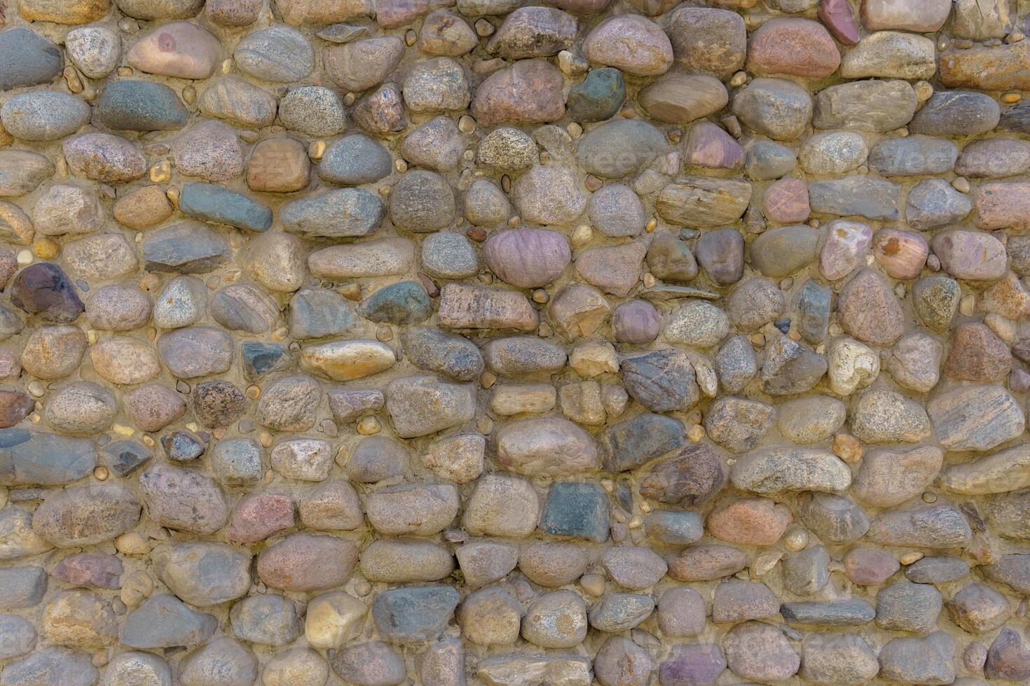 Wall fence of stones of different sizes roughly stacked on top of each other and fastened with cement. Industrial background. photo