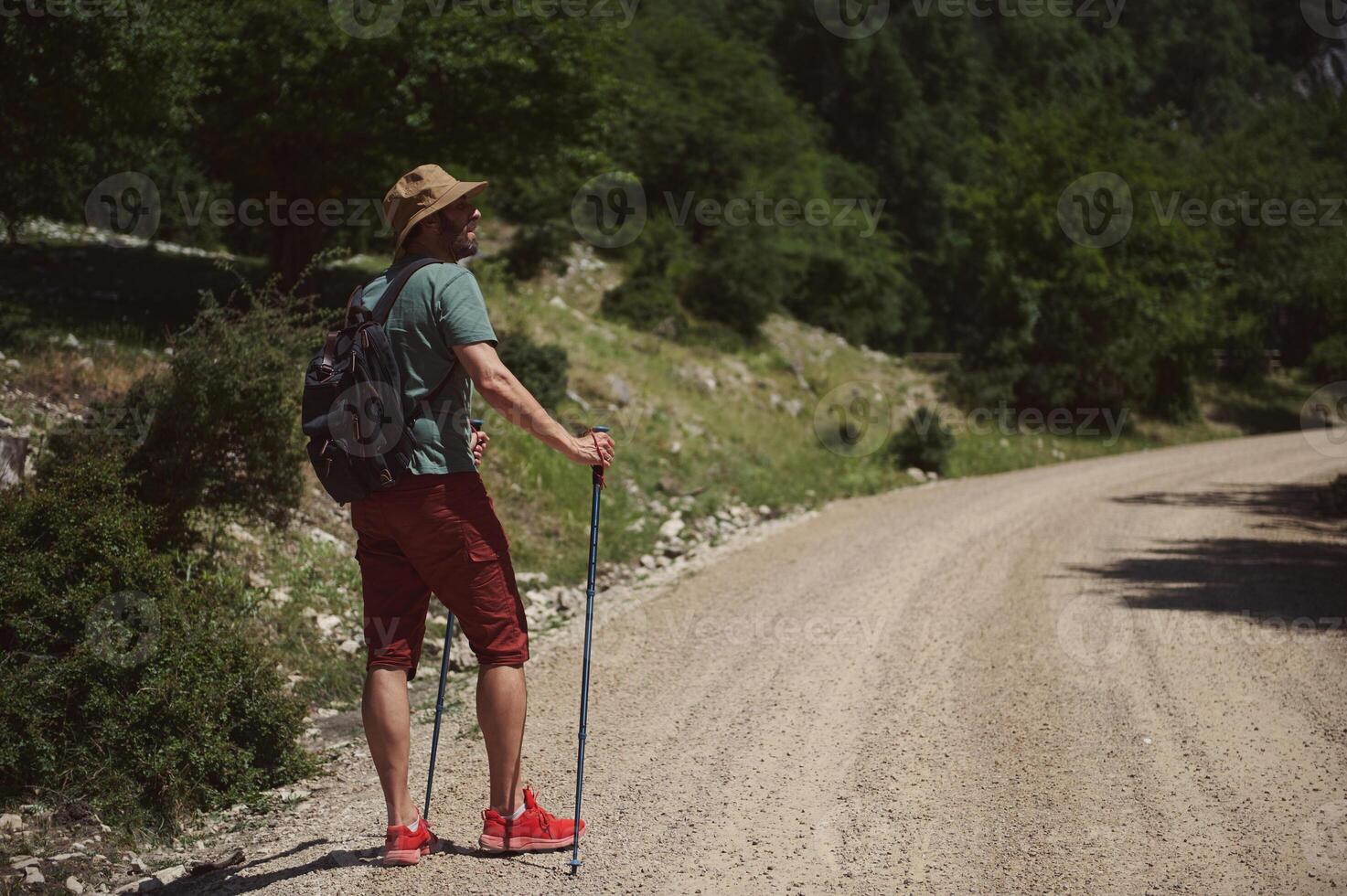 Man Hiking Along a Sunny Mountain Trail with Backpack and Trekking Poles photo