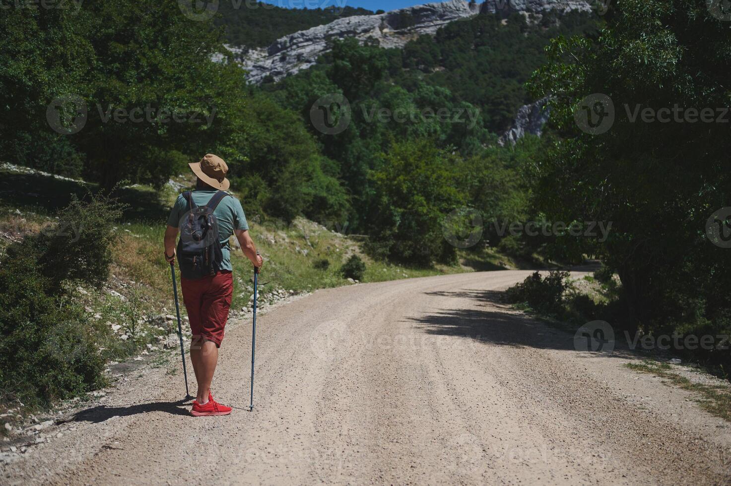 Man Hiking Along a Mountain Path with Walking Sticks and Backpack photo