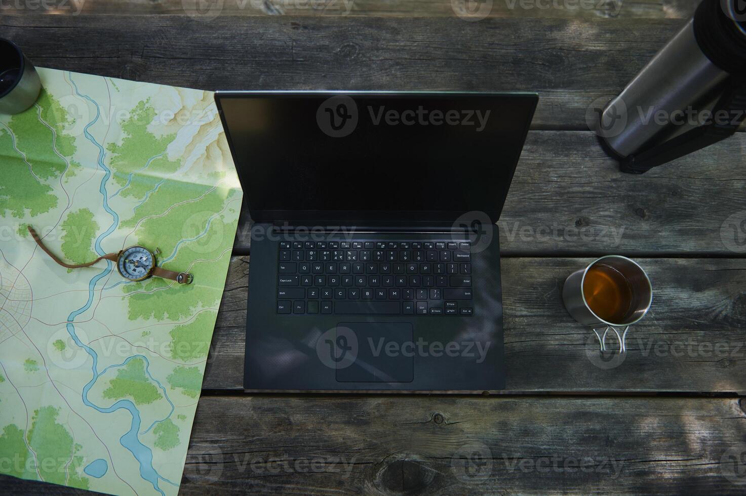 Outdoor Workstation Setup with a Laptop, Map, Compass, and Tea photo