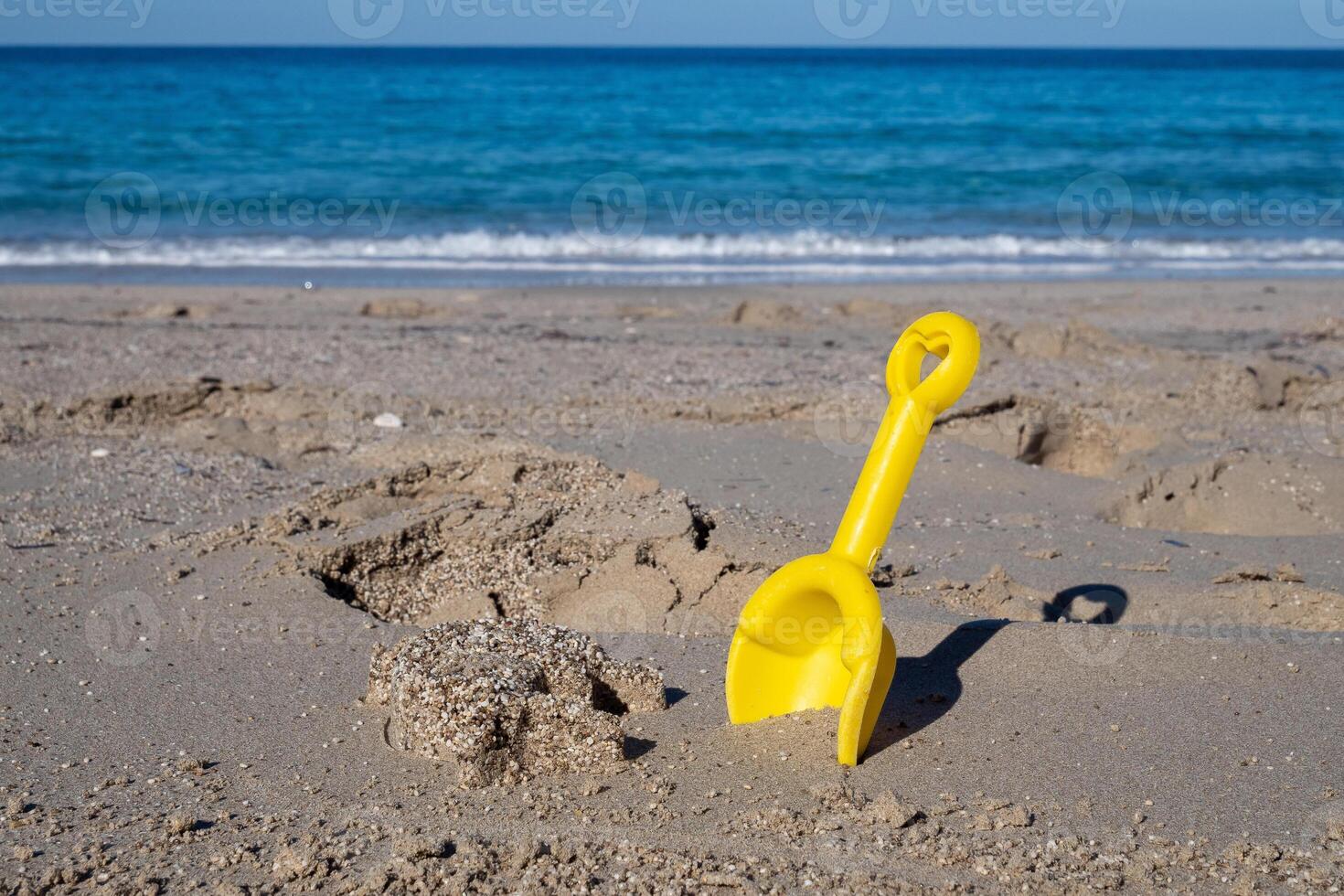 Yellow plastic shovel for playing in the sand on a beach with turquoise sea photo