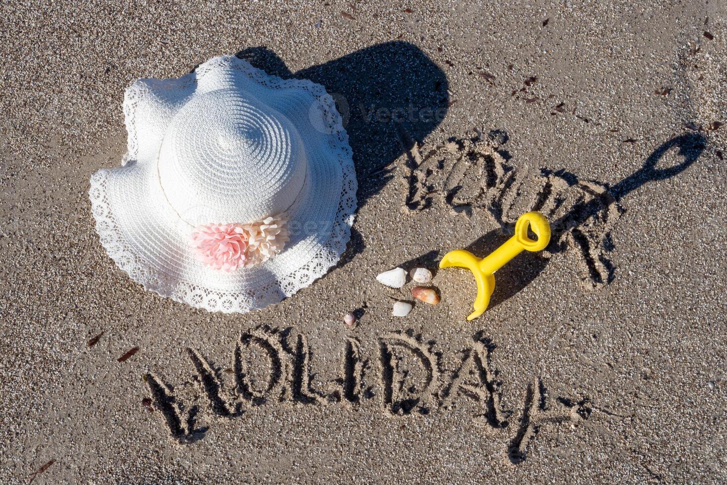 Holiday sign and toys on sandy beach with sun hat photo