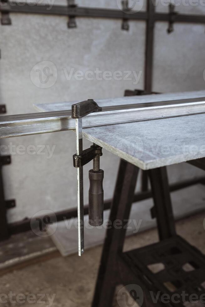 Fixing a square metal pipe with a metal clamp and a sheet of straight slate on a workbench at a construction site photo