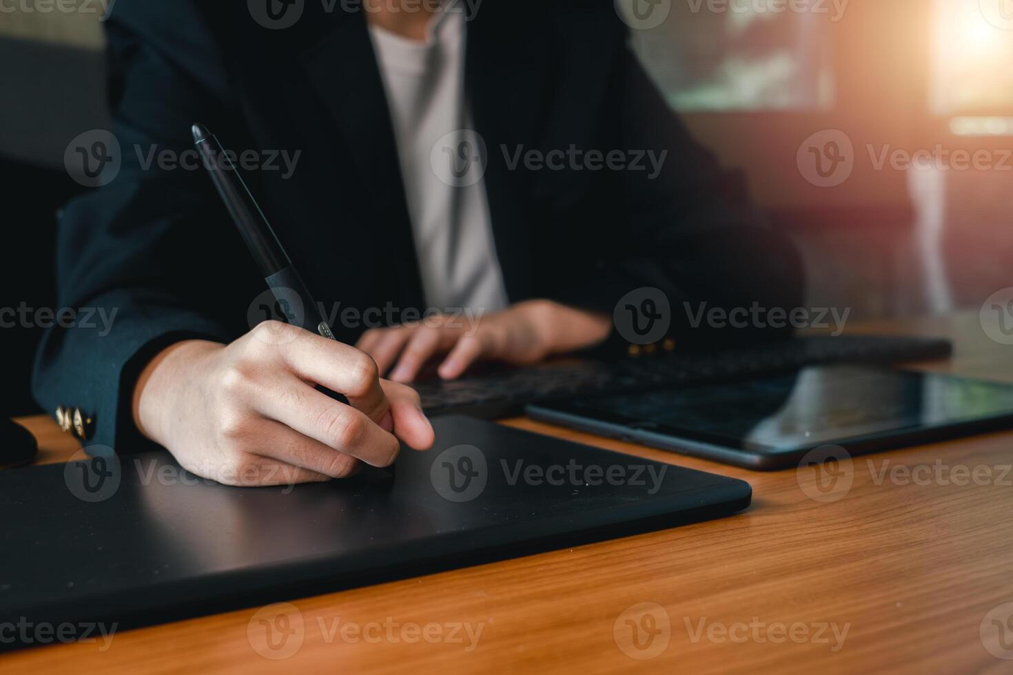 A person in a suit using a digital tablet and stylus at a wooden desk, highlighting modern technology in a professional environment. photo