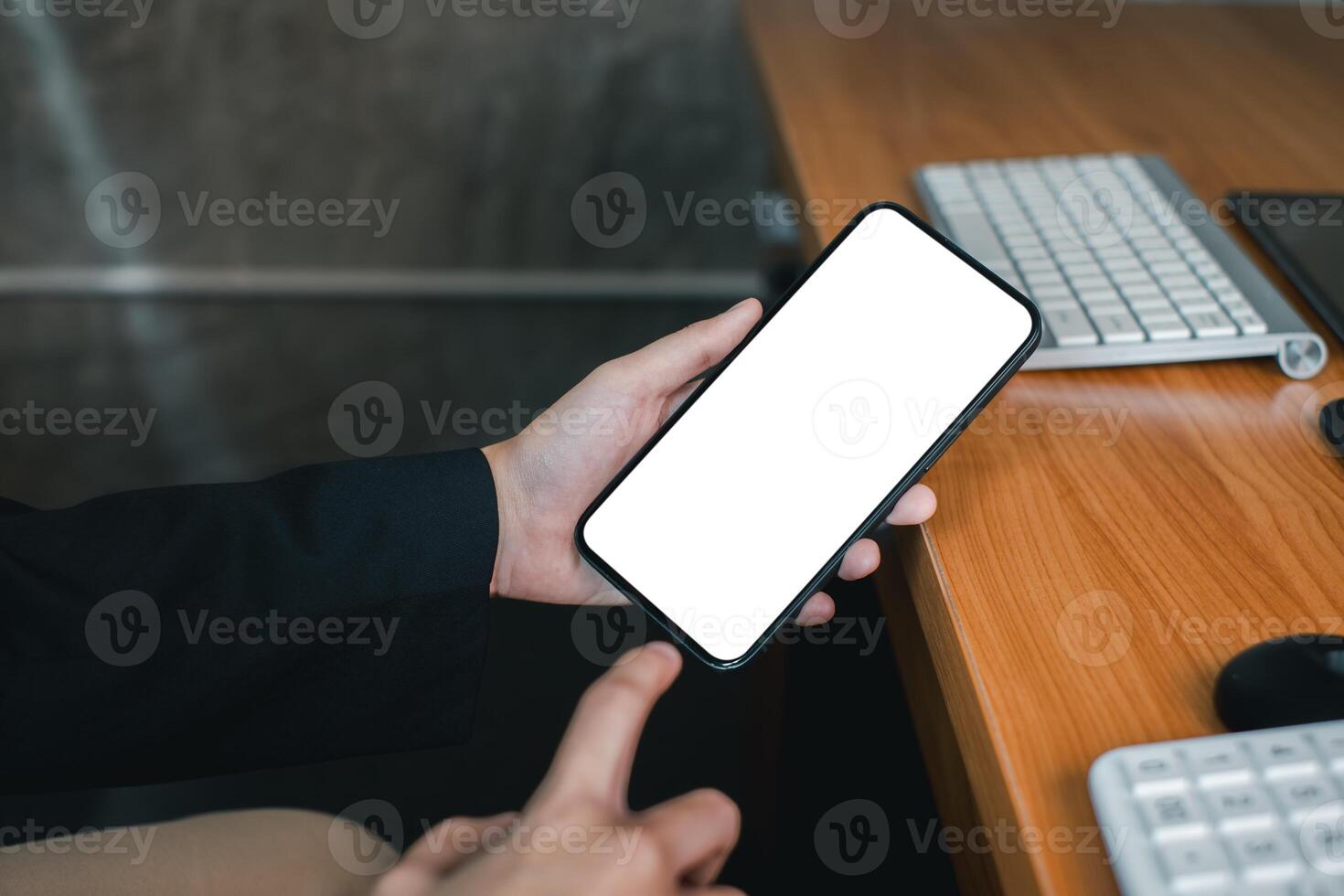 Professional holding a smartphone with a blank screen at a wooden office desk, ideal for app or website mockup. photo