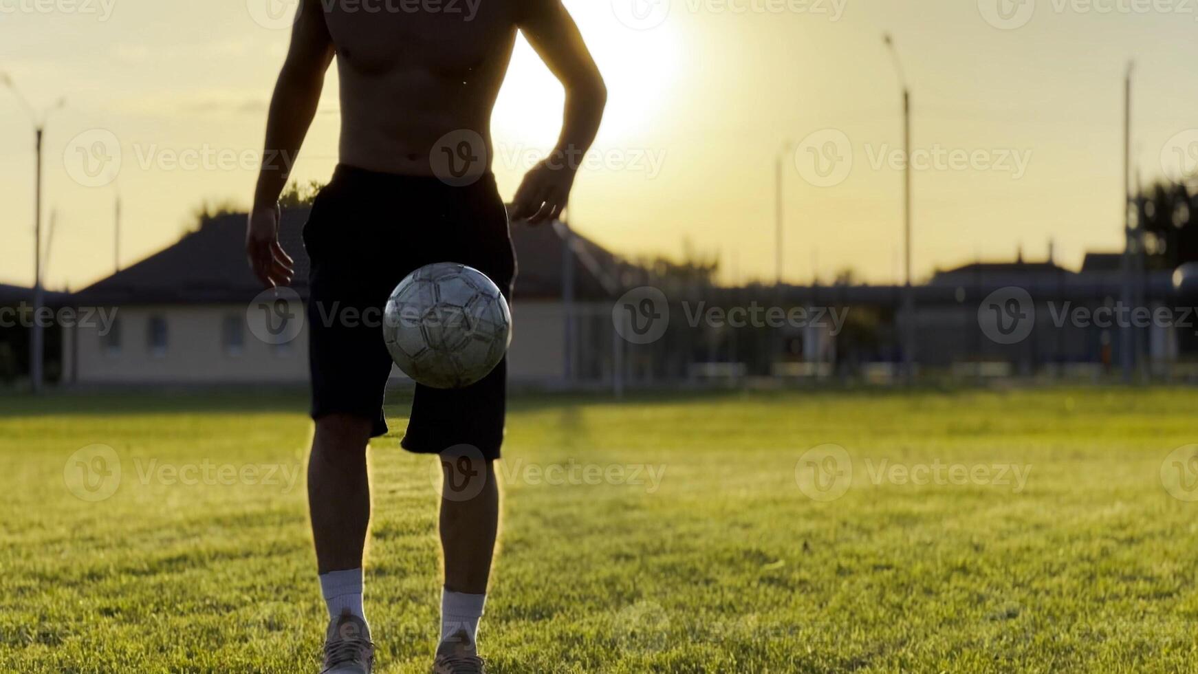 Male feet of professional footballer kicking ball at green field.Legs of young man juggling soccer ball on stadium at sunset. Sportsman practicing tricks outdoor. Freestyle football concept photo