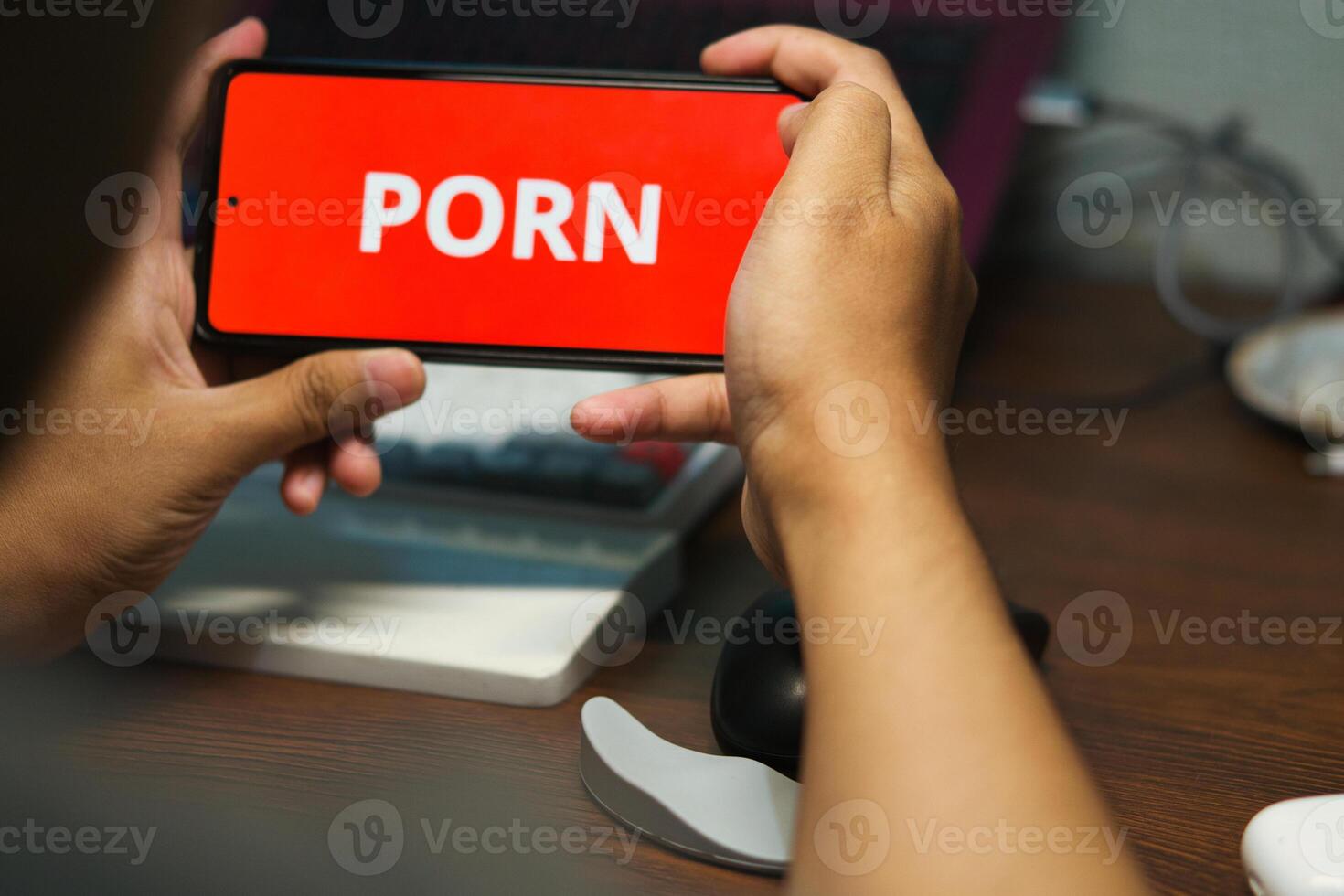 Hand Holding Smartphone with Written on Red Background. A Concept Illustration of a Person Addicted to Watching Adult photo