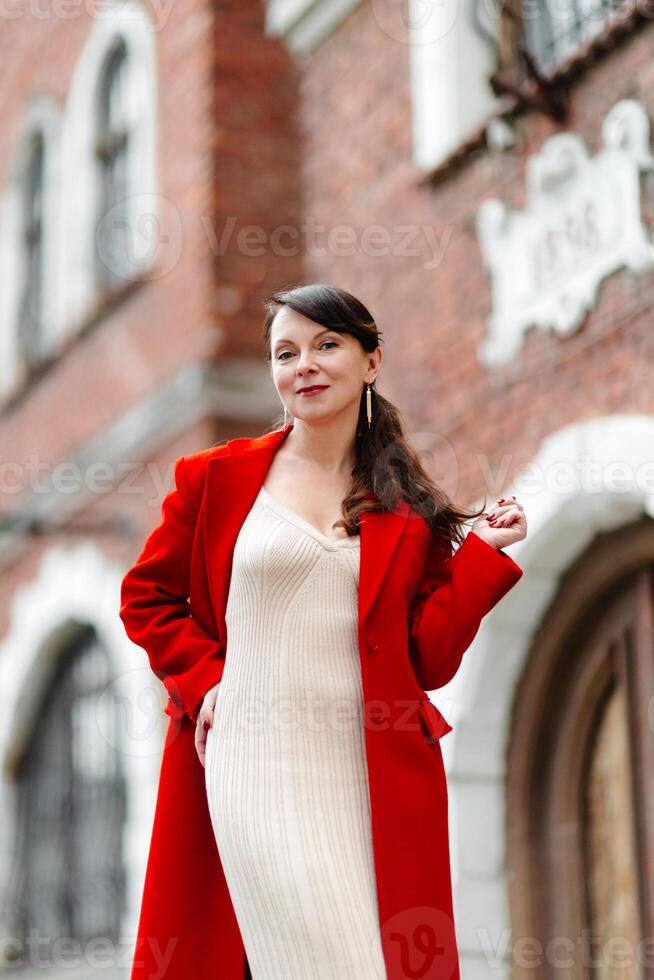 Elegant businesswoman wearing red jacket standing at a low wall. photo