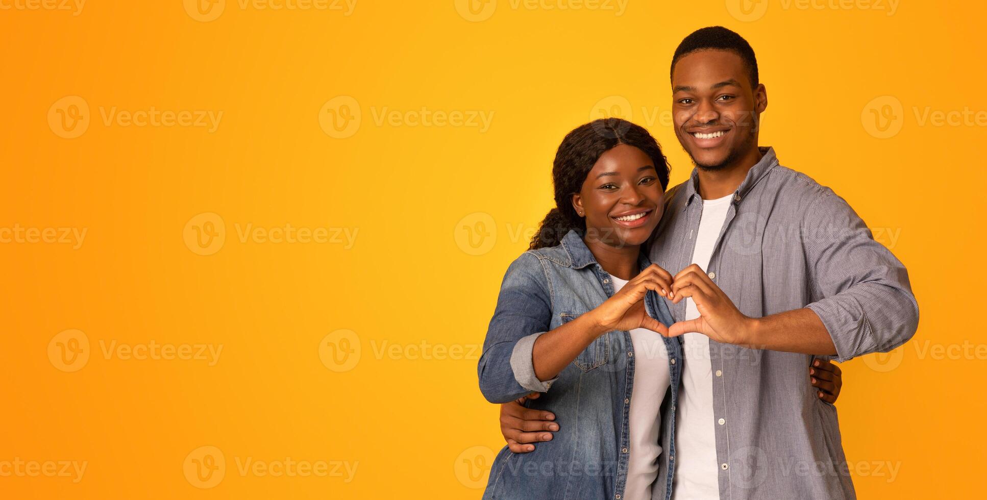Portrait Of Happy Romantic Black Couple Making Heart Gesture Together, Connecting Their Hands Into Love Sign, African American Man And Woman Smiling At Camera While Posing Over Yellow Background photo