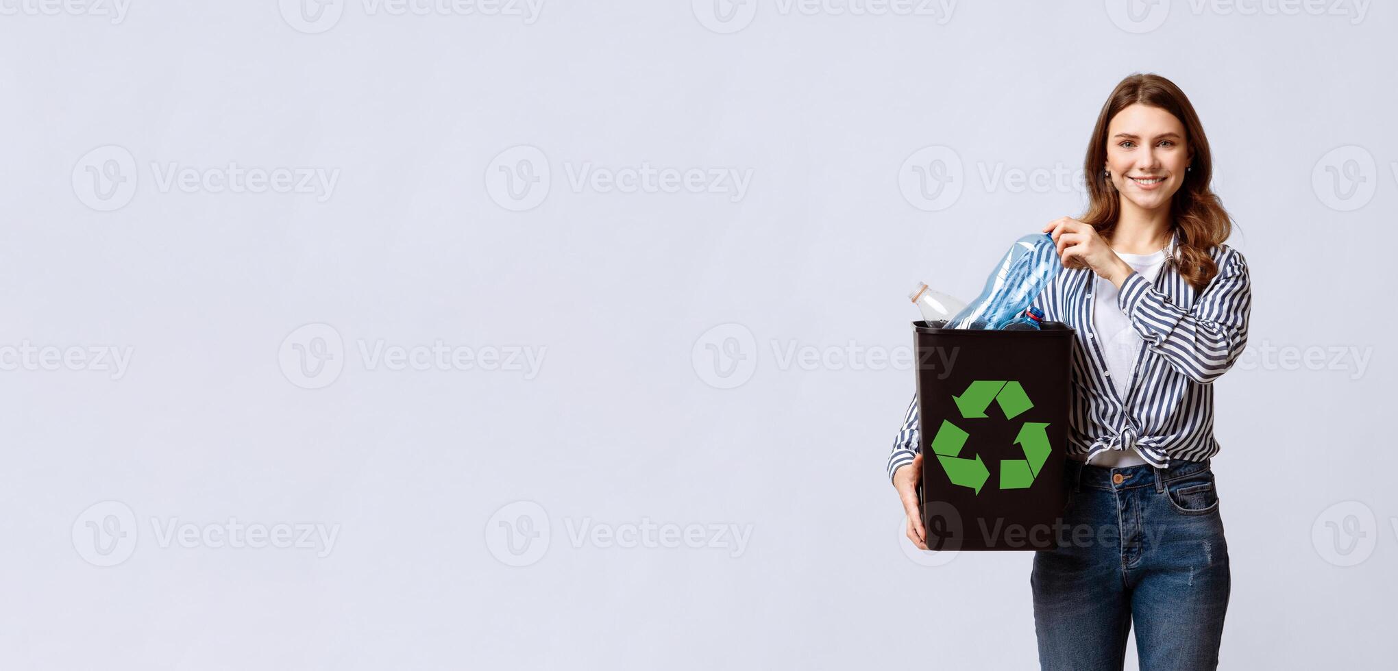 A woman stands confidently holding a container filled with recyclable materials. She promotes an eco-friendly lifestyle with enthusiasm, copy space photo