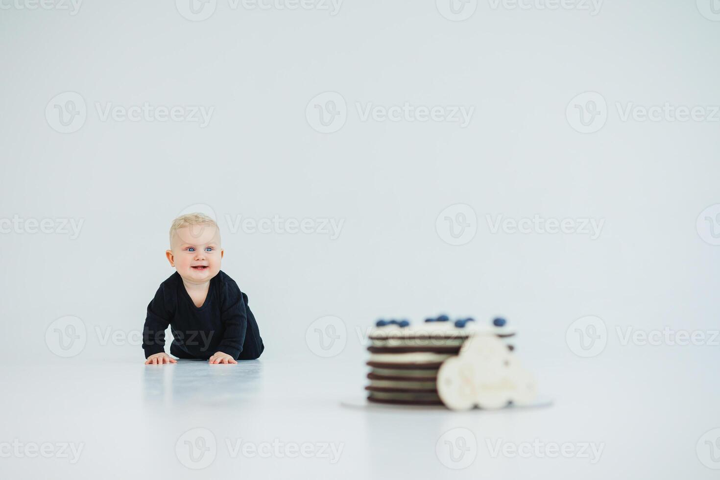 An adorable and cute baby is crawling eagerly towards a delicious birthday cake placed beautifully on a minimalist white background, creating a joyful scene perfect for capturing a delightful moment photo