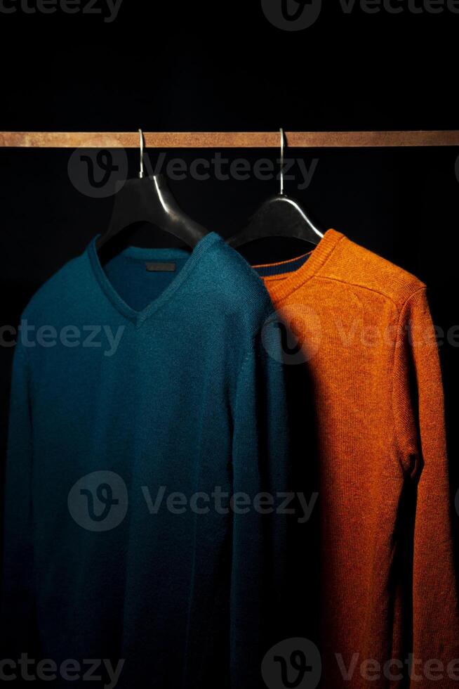 Plain Orange And Teal Sweatshirts on Hanger, Isolated on Black Background photo