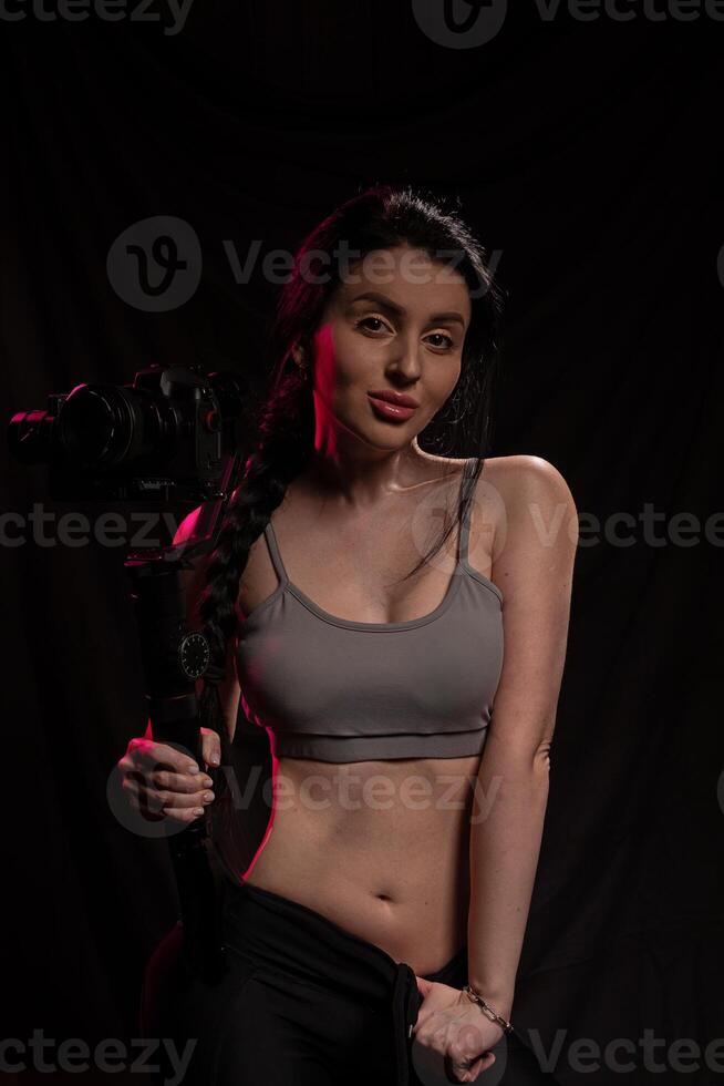 Young woman with camera strikes a confident pose in a dimly lit studio setting photo