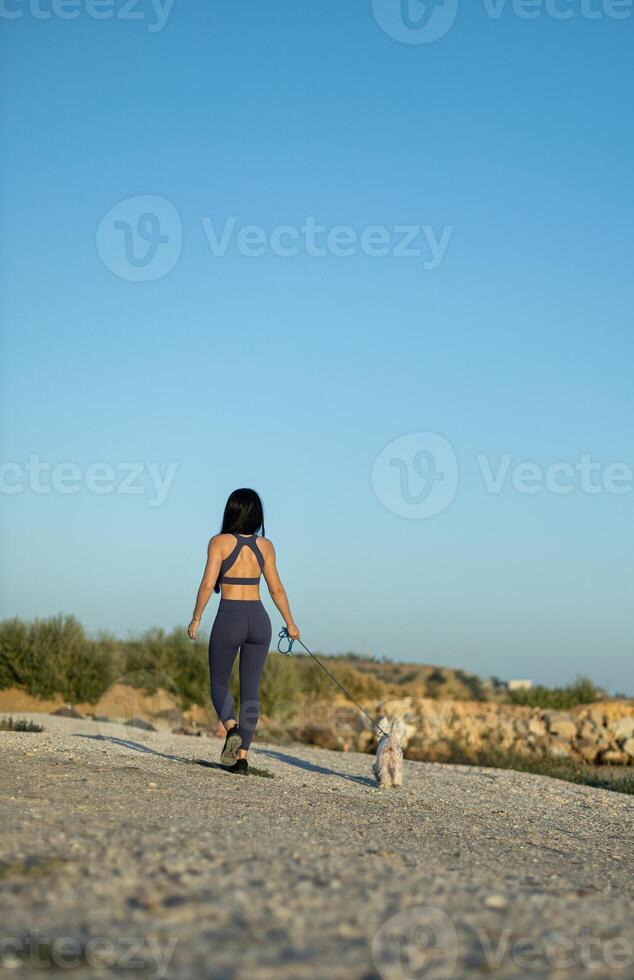 Brunette woman walks on beach with white dog while enjoying sunny day and practicing epilation photo
