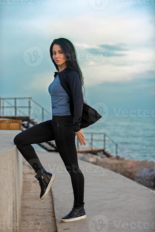 Young woman stretching by the ocean during a sunny afternoon near a coastal pathway photo