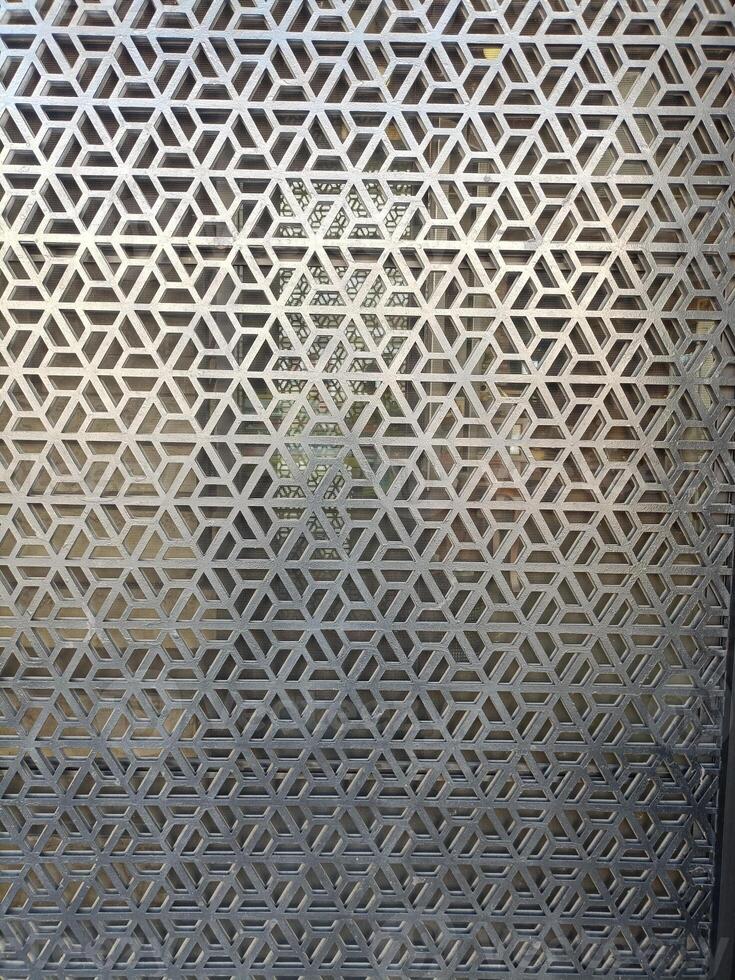 Image shows decorative metal screen with geometric pattern, creating layered visual effect with silhouette of person behind it, adding depth and artistic appeal photo
