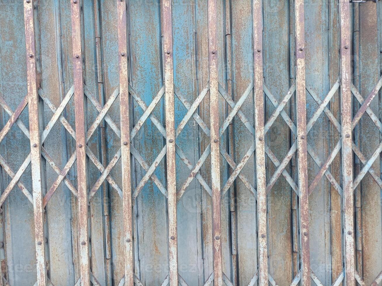 Rusty metal gate with crisscross pattern and weathered blue paint, showing signs of age and exposure to elements, creating textured and industrial appearance photo