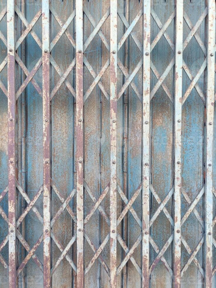 Rusty metal gate with crisscross pattern and peeling paint old and weathered surface blue and brown tones vertical and diagonal lines industrial style textured background vintage appearance photo