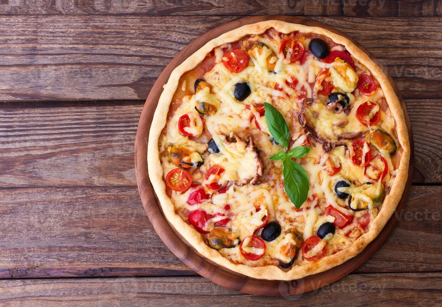 A pizza on a wooden table with a green leaf photo