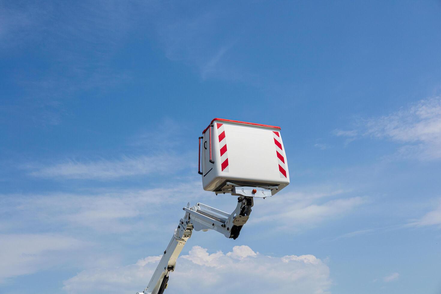A utility vehicle raises its platform against a clear blue sky with a few clouds, likely for maintenance or installation work photo