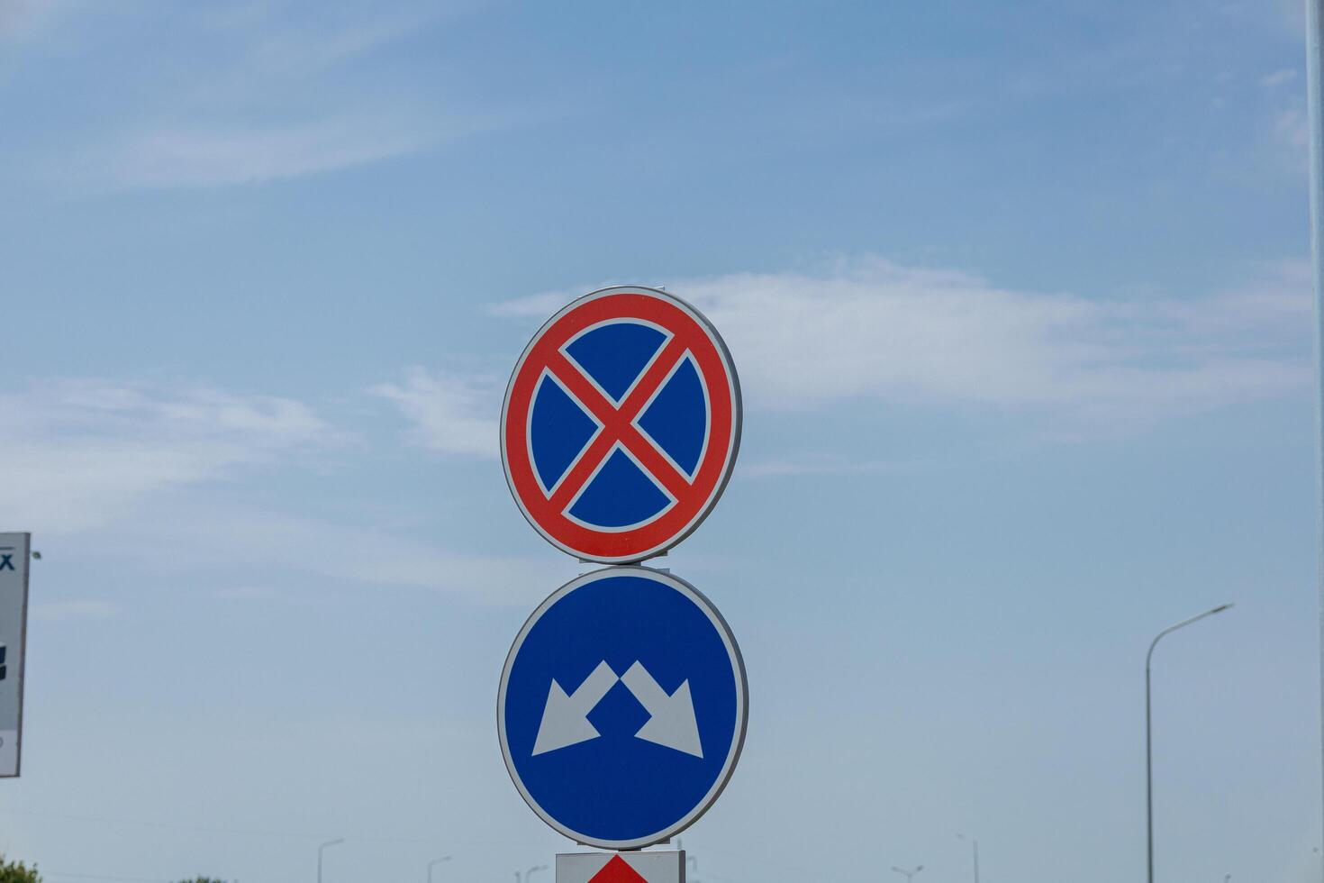 A no parking sign and a directional arrow are positioned along a road under a clear blue sky with minimal clouds photo