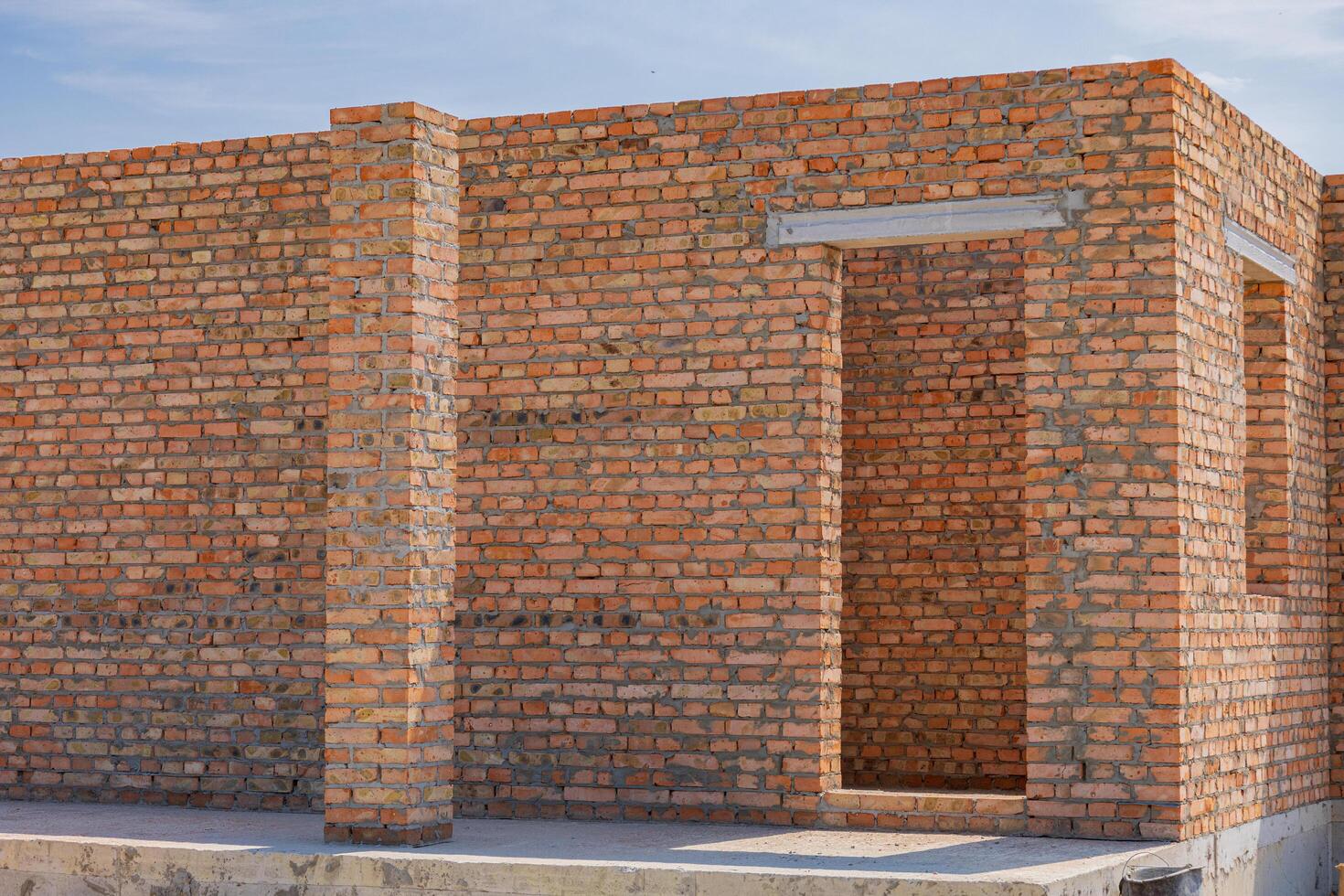 Construction of a brick structure is underway, showcasing raw, unfinished walls and an open doorway in bright sunlight photo