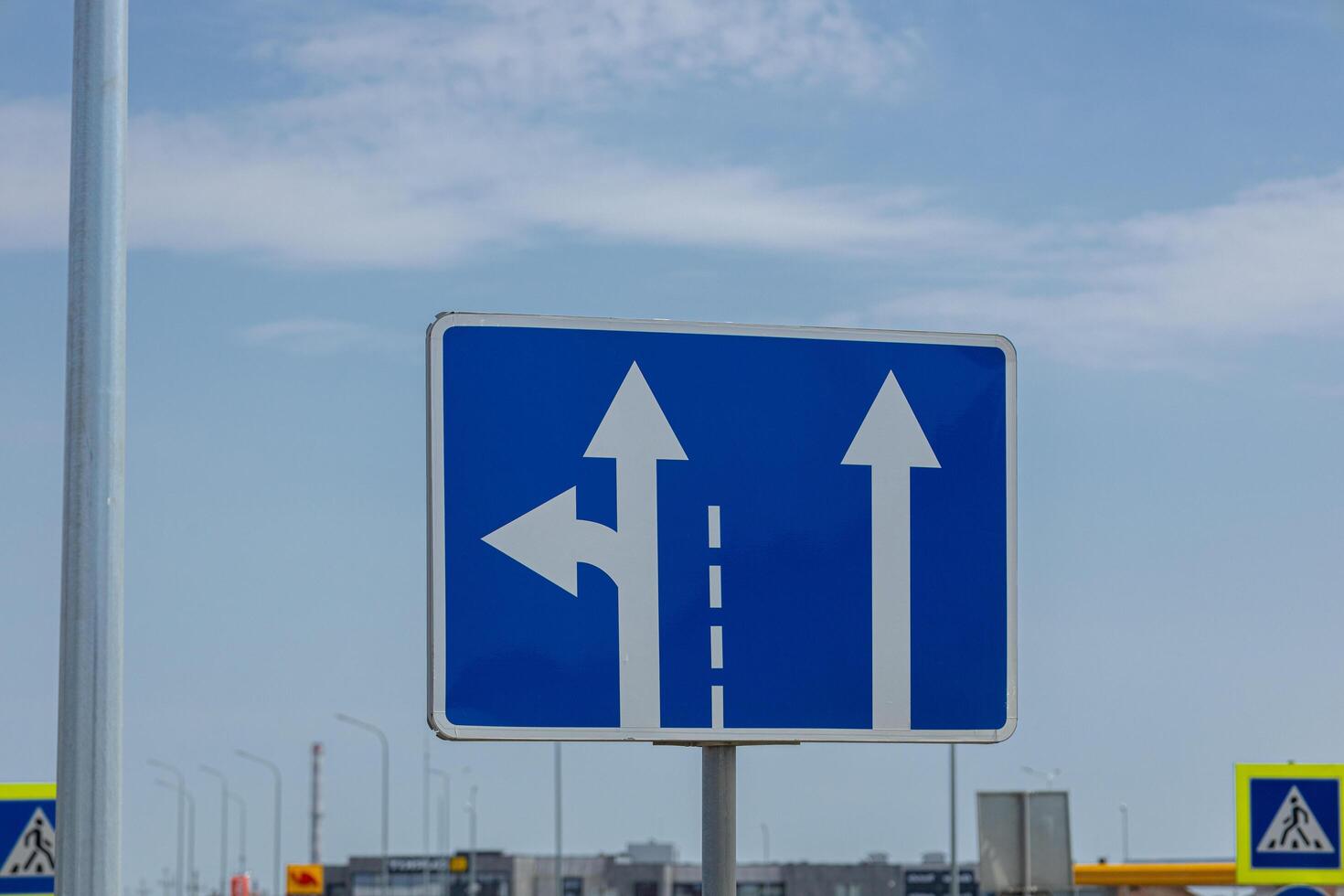 A road sign displays arrows pointing straight and left, guiding drivers at an intersection under a blue sky photo