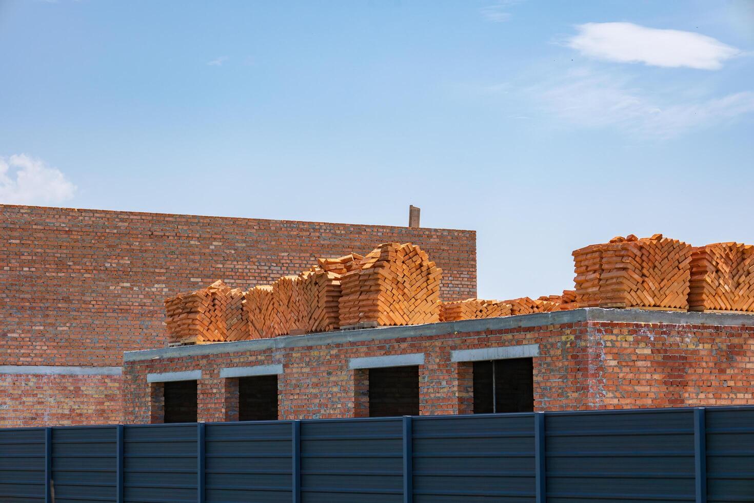 Workers are preparing a building structure with numerous bricks neatly piled on top of a partially completed wall photo