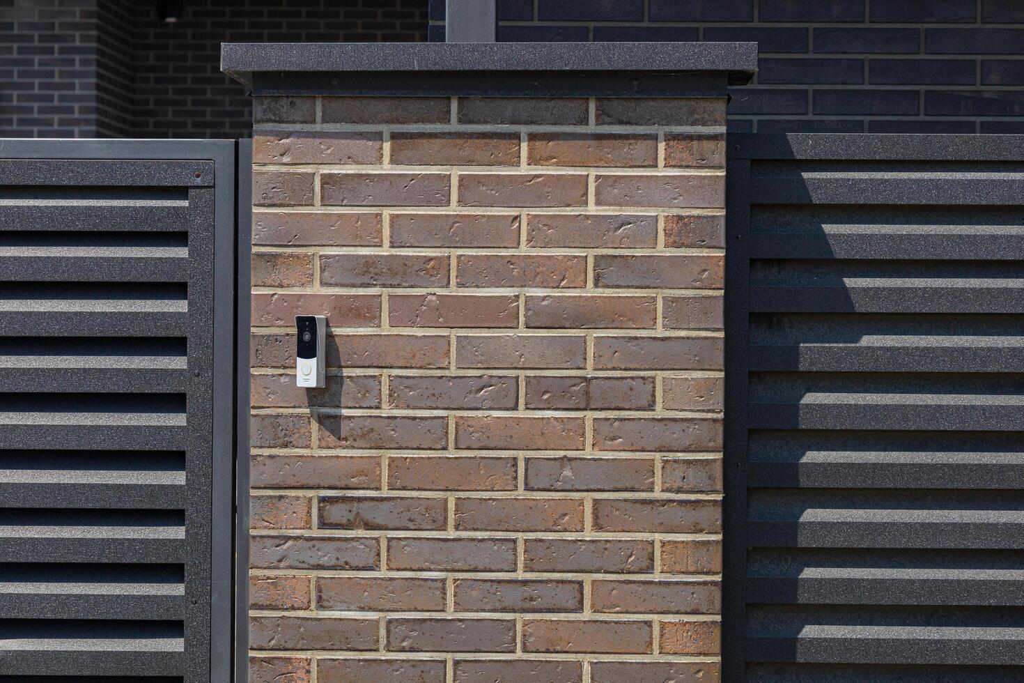 An intercom is mounted on a stylish brick wall at the entrance of a contemporary home, providing communication access for visitors photo